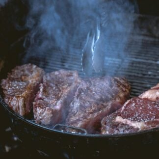 Four chuck steaks cooking on a grill.