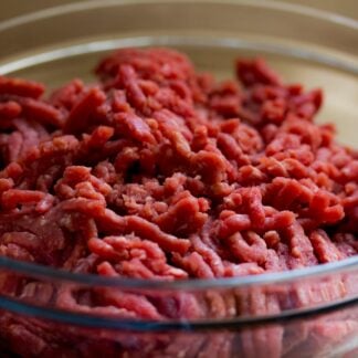 Fresh uncooked grass-fed ground beef in glass bowl.